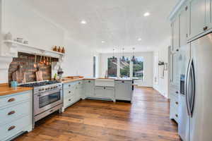 Kitchen with a peninsula, a textured ceiling, appliances with stainless steel finishes, dark wood-style flooring, and open shelves