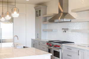 Kitchen with open shelves, high end appliances, wall chimney exhaust hood, decorative backsplash, and pendant lighting