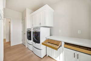 Laundry area with washing machine and dryer, light wood-style flooring, and cabinet space