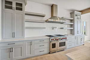 Kitchen with open shelves, wall chimney range hood, range with two ovens, tasteful backsplash, and light wood-style flooring
