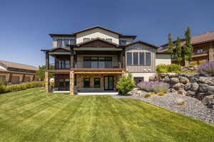 Back of house with a balcony, board and batten siding, a lawn, and a patio area