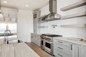Kitchen featuring open shelves, premium appliances, exhaust hood, tasteful backsplash, and light stone countertops