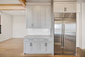 Kitchen featuring stainless steel built in refrigerator, light wood finished floors, light stone counters, gray cabinetry, and tasteful backsplash