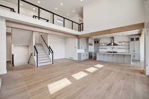 Unfurnished living room with recessed lighting, stairs, light wood-style floors, and a towering ceiling