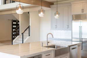 Kitchen featuring built in fridge, decorative light fixtures, and light stone counters