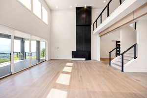 Unfurnished living room featuring stairway, light wood finished floors, a towering ceiling, french doors, and recessed lighting
