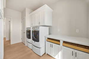 Laundry area with washing machine and dryer, light wood-style flooring, and cabinet space