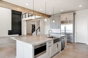 Kitchen with stainless steel appliances, light stone counters, light wood-type flooring, a center island with sink, and recessed lighting