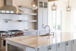 Kitchen featuring premium range, wall chimney range hood, tasteful backsplash, glass insert cabinets, and light stone counters