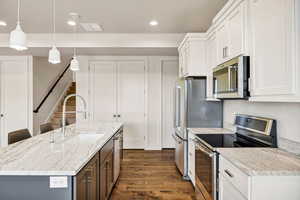 Kitchen featuring stainless steel appliances, a kitchen island with sink, white cabinetry, dark wood-style floors, and light stone countertops