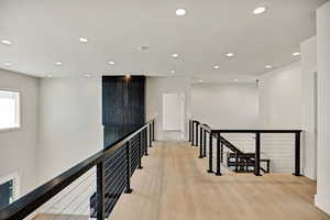 Hallway with an upstairs landing, light wood-type flooring, and recessed lighting