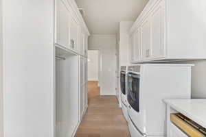 Laundry area with independent washer and dryer, cabinet space, and light wood-style flooring