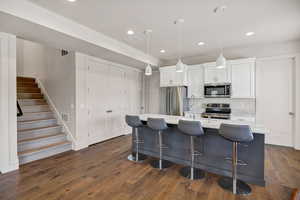 Kitchen with recessed lighting, appliances with stainless steel finishes, a kitchen island with sink, white cabinetry, and dark wood-style floors