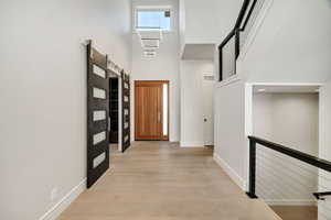 Hallway featuring light wood-type flooring, a towering ceiling, and a barn door