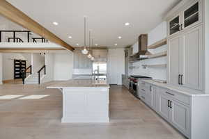 Kitchen featuring wall chimney range hood, premium appliances, recessed lighting, light wood-type flooring, and a center island with sink