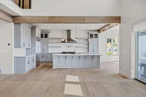 Kitchen featuring gray cabinets, light countertops, wall chimney range hood, an island with sink, and recessed lighting