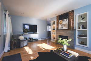 Living area with a large fireplace, wood finished floors, built in shelves, and recessed lighting