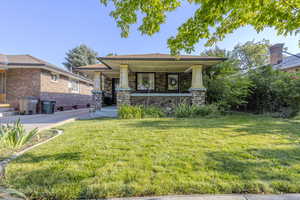 View of front of property with a porch, a front lawn, and stone siding
