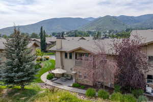 Back of property with stucco siding, a patio area, a balcony, a chimney, and stone siding