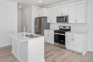 Kitchen featuring stainless steel appliances, white cabinetry, light countertops, a center island with sink, and recessed lighting