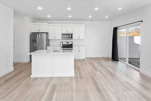 Kitchen with recessed lighting, an island with sink, white cabinetry, stainless steel appliances, and light countertops