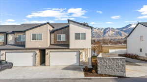 View of front of home with stone siding, an attached garage, driveway, and a shingled roof
