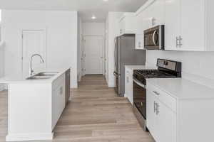 Kitchen with stainless steel appliances, white cabinetry, a center island with sink, light countertops, and recessed lighting