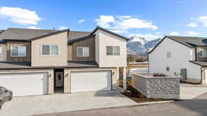 View of front of property with an attached garage, stone siding, driveway, a mountain view, and a shingled roof