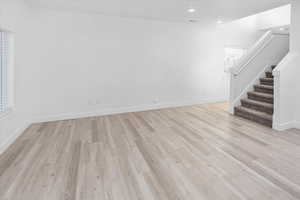Unfurnished living room with stairs, light wood-type flooring, and recessed lighting