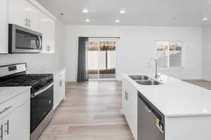 Kitchen with stainless steel appliances, light wood-style floors, recessed lighting, a center island with sink, and white cabinetry