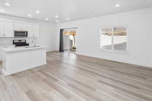 Kitchen with recessed lighting, appliances with stainless steel finishes, light countertops, a center island with sink, and light wood finished floors