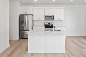 Kitchen featuring stainless steel appliances, white cabinetry, light countertops, recessed lighting, and a kitchen island with sink