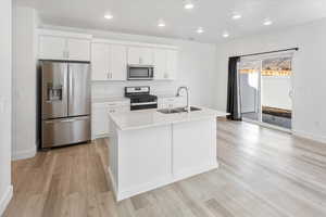 Kitchen featuring appliances with stainless steel finishes, white cabinets, recessed lighting, light countertops, and an island with sink