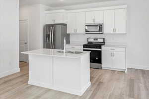 Kitchen with appliances with stainless steel finishes, white cabinets, light countertops, an island with sink, and light wood finished floors