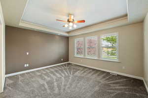 Spare room featuring a raised ceiling, carpet floors, and ceiling fan