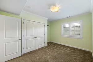 Unfurnished bedroom featuring dark carpet, crown molding, and a closet