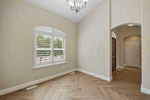 Spare room featuring arched walkways, a chandelier, and high vaulted ceiling