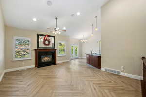 Unfurnished living room featuring a ceiling fan, a fireplace with flush hearth, a chandelier, recessed lighting, and high vaulted ceiling