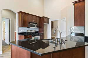 Kitchen with tasteful backsplash, appliances with stainless steel finishes, arched walkways, a peninsula, and a towering ceiling