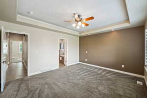 Unfurnished bedroom with a tray ceiling, carpet, ensuite bath, and a ceiling fan