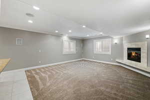 Unfurnished living room with recessed lighting, a tiled fireplace, ornamental molding, and light colored carpet