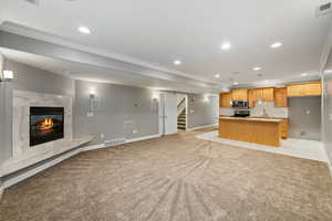 Kitchen featuring open floor plan, crown molding, light colored carpet, recessed lighting, and a premium fireplace