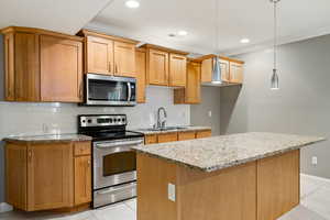 Kitchen with appliances with stainless steel finishes, ornamental molding, tasteful backsplash, light tile patterned flooring, and light stone countertops
