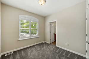 Unfurnished bedroom with dark colored carpet and connected bathroom