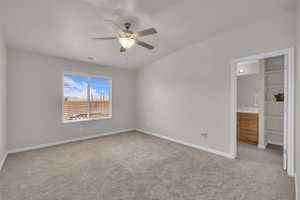 Unfurnished bedroom featuring light colored carpet, a ceiling fan, connected bathroom, and lofted ceiling