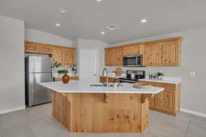 Kitchen with appliances with stainless steel finishes, light countertops, a kitchen island with sink, a breakfast bar, and recessed lighting