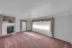 Unfurnished living room with carpet flooring, a fireplace, a textured ceiling, a chandelier, and ornamental molding