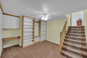 Basement featuring light carpet, a ceiling fan, a textured ceiling, and stairway