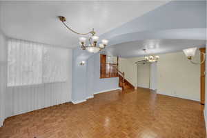 Unfurnished living room featuring a chandelier, a textured ceiling, stairway, and plenty of natural light