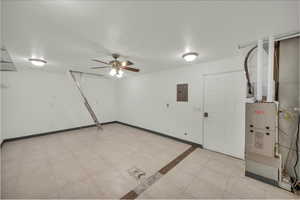 Below grade area with electric panel, ceiling fan, heating unit, and light tile patterned floors